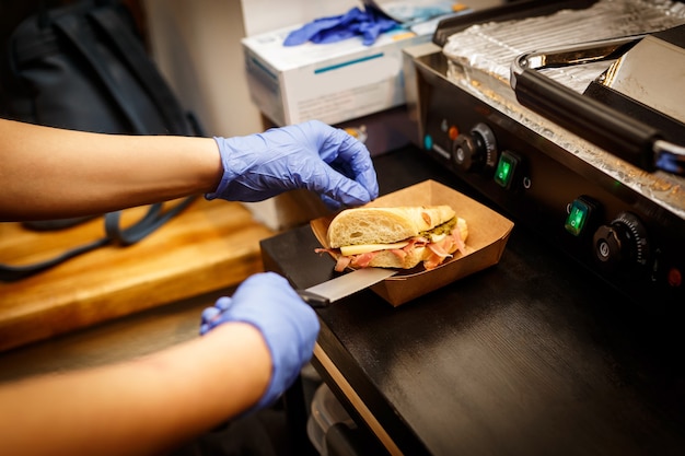 Sandwich in blauen Handschuhen machen.