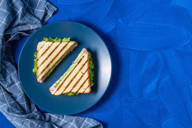 Sándwich de jamón y verduras sobre un fondo azul.