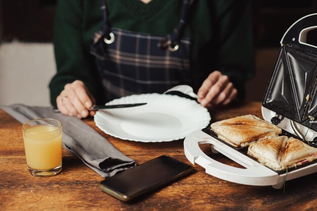 Sándwich y jugo Preparación de bocadillos y desayuno Sandwichera y mujer irreconocible sobre fondo de madera