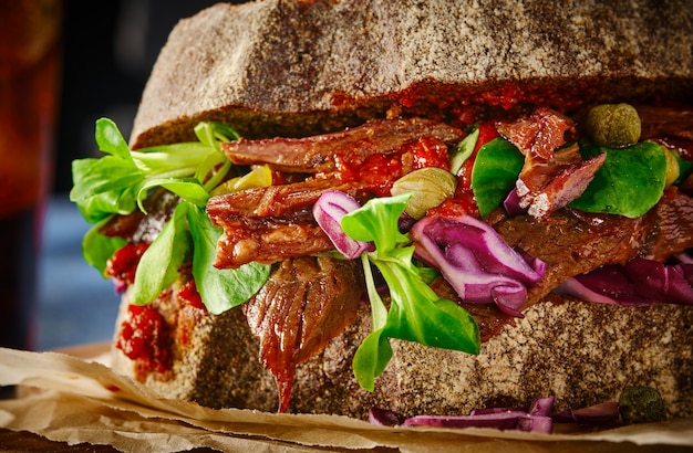 Sándwich jugoso de ternera a la parrilla con verduras, alcaparras y col y salsa. De cerca.