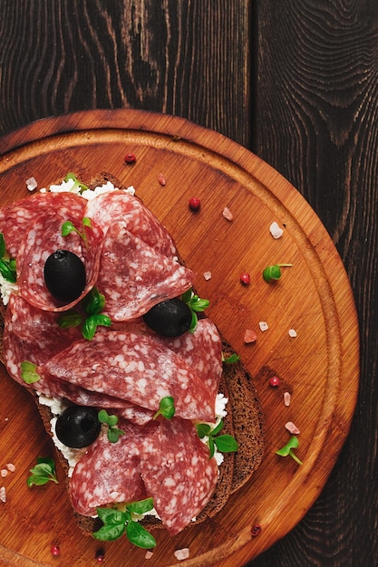 Sandwich-Körnerbrot mit Frischkäse und Salami schwarze Oliven Microgreens Draufsicht Nahaufnahme keine Personen Frühstück