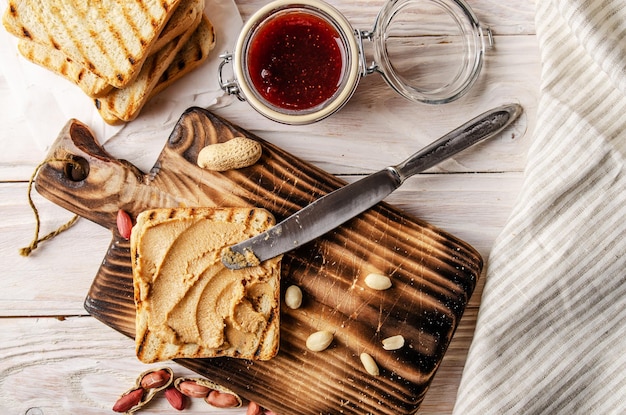 Sándwich de mantequilla de maní con vista de ángulo bajo en la tabla de cortar con tostadas y mermelada a un lado. Concepto de alimentación saludable