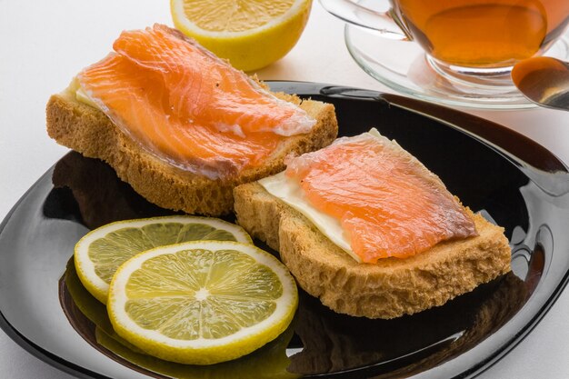 Sandwich de mantequilla, salmón salado y limón en un plato negro