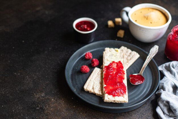 sándwich de mermelada y taza de café mermelada de bayas dulces mantequilla pan de dieta de grano entero crujiente sobre la mesa