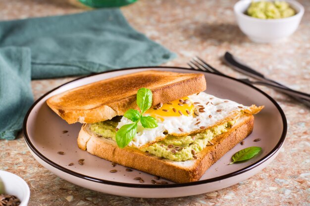 Sandwich mit Avocado-Spiegelei und Leinsamen auf Toast auf einem Teller auf dem Tisch