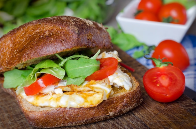 Sandwich mit dunklem Brot, Eiern, Tomaten und Rucola.