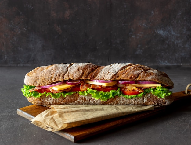 Sandwich mit dunklem Brot mit Salat, Speck, Tomaten, Käse und Zwiebeln. Frühstück. Fast Food.