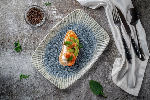 Sandwich mit gebratenen Garnelen und Avocado auf einem Teller mit Grüns vor einem grauen Steintisch