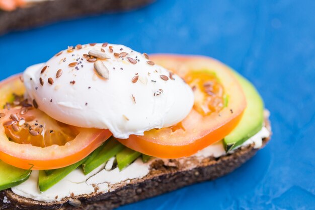 Sandwich mit geräuchertem Lachs, Ei und Avocado auf blauer Oberfläche, Nahaufnahme. Konzept für eine gesunde Ernährung