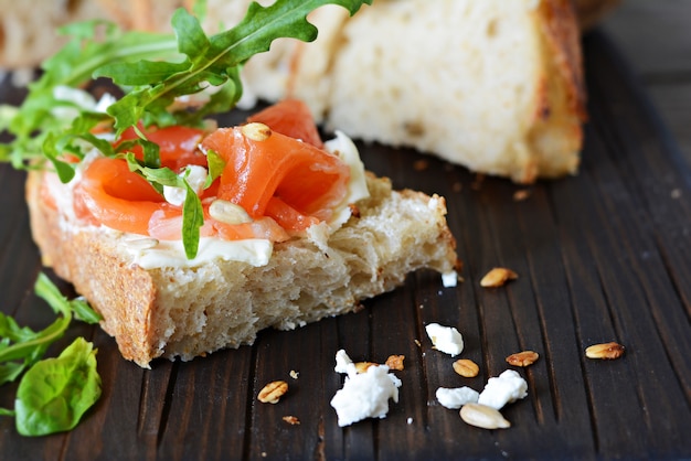 Sandwich mit leicht gesalzenem Lachs, Rucola, Samen und Hüttenkäse auf dem Brett. Sauerteigbrot Toast mit gesalzenem Fisch, Smorrebrod.