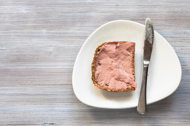 Sandwich mit Pastete und Messer auf weißer Platte