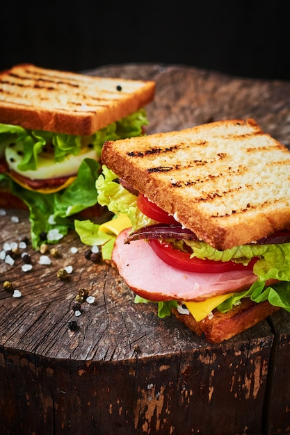 Sandwich mit Salat, Schinken, Tomaten und Zwiebeln auf dunklem Hintergrund