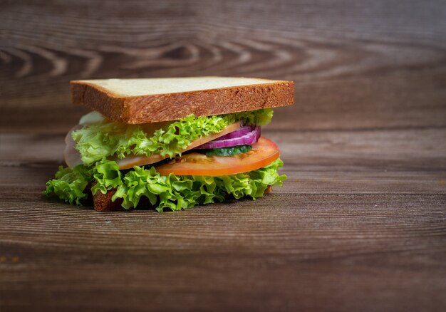 Sandwich mit Schinken, Tomaten und grünem Salat auf einem dunklen Tisch.