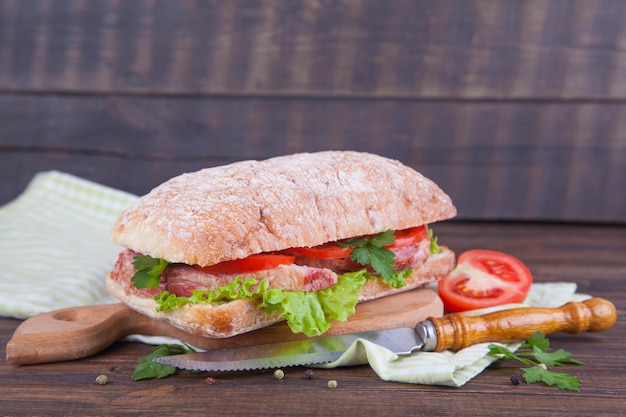 Sandwich mit Schinken und Gemüse auf einem dunklen hölzernen Hintergrund.