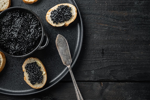 Sandwich mit schwarzem Kaviar und Butter auf Draufsicht des schwarzen Holztischhintergrundes lag flach mit Kopienraum für Text Beschneidungspfad eingeschlossen