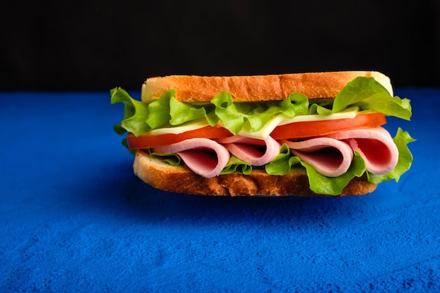 Sandwich mit Speck, Käse und Kräutern auf einer blauen Oberfläche