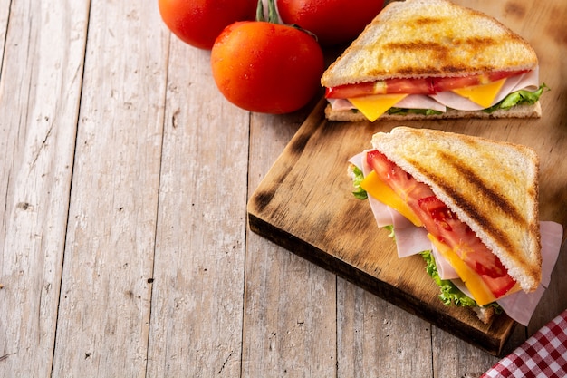 Sandwich mit Tomaten, Salat, Schinken und Käse auf Holztisch