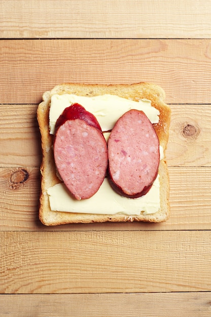 Sandwich mit Wurst auf Holzhintergrund. Ansicht von oben