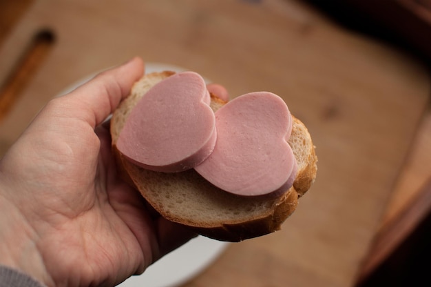 Sandwich mit Wurst in Form von Herzen in der Hand auf verschwommenem Hintergrund