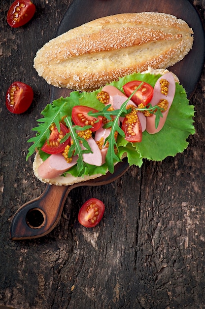 Sandwich mit Wurst, Kopfsalat, Tomate und Arugula auf der alten Holzoberfläche