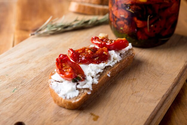 Sandwich mit Ziegenkäse, sonnengetrockneten Tomaten und Thymian, serviert auf dem Brett an einer hellen Holzoberfläche