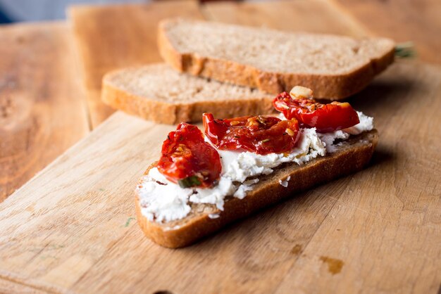 Sandwich mit Ziegenkäse, sonnengetrockneten Tomaten und Thymian, serviert auf dem Brett an einer hellen Holzoberfläche