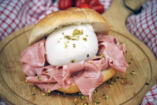 Foto sándwich con mozzarella mortadella y pistachos picados en una tabla de cortar de madera