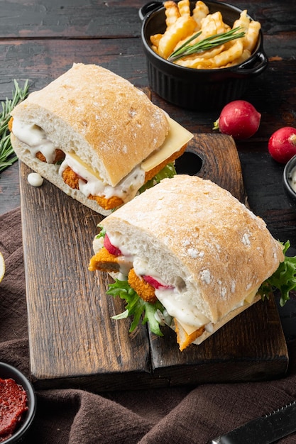 Sándwich con palitos de pescado sobre tabla de cortar de madera sobre fondo de mesa de madera oscura antigua