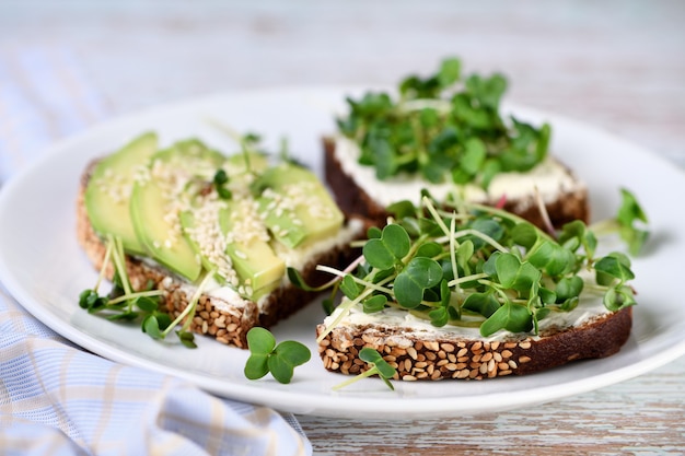 Sándwich de pan de centeno con cereales, queso crema, aguacate y brotes de rábano germinados (microverdes)