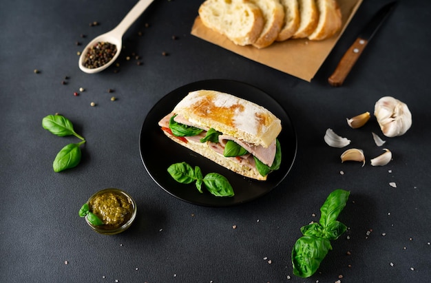 Sándwich de pan ciabatta con salsa de pesto de jamón Tomates Albahaca sobre un fondo negro Alimentos Alimentos backgroun