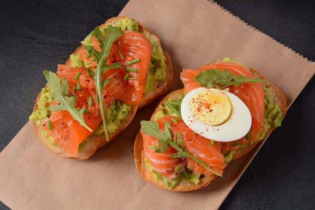 Sándwich de pan integral con pasta de aguacate y hojas de salmón, huevo y rúcula