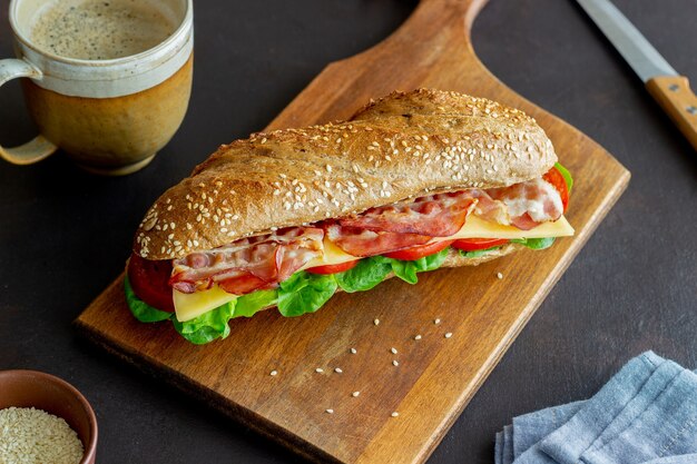 Un sándwich de pan negro con ensalada, tocino, tomate y queso. Desayuno. Comida rápida.