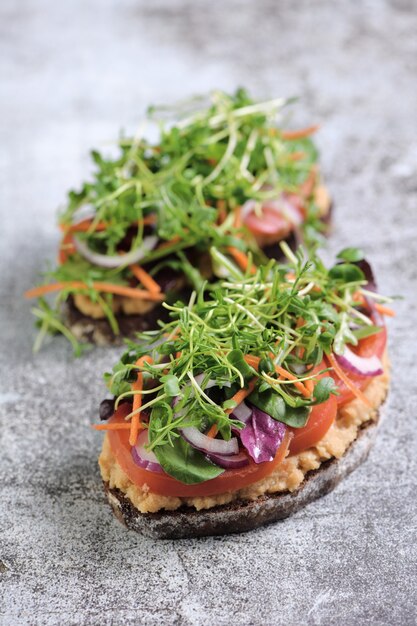 Sandwich de pan rústico tostado con garbanzos hummus rodajas de tomate mezcla de lechuga y microgreens