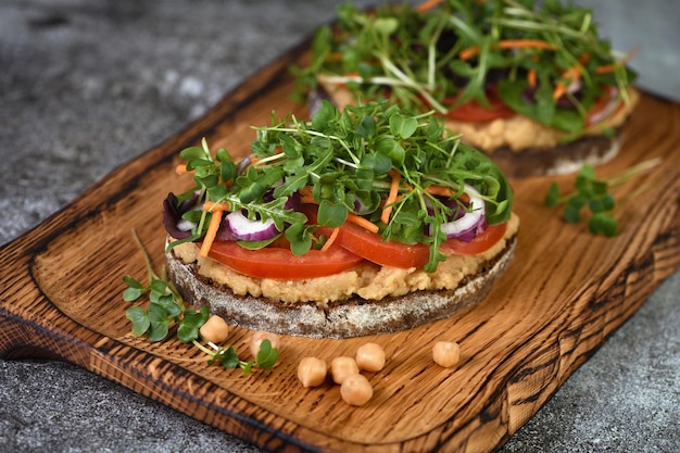 Sándwich de pan rústico tostado con hummus de garbanzos, rodajas de tomate, mix de lechugas y microgreens. Desayuno vegetariano.