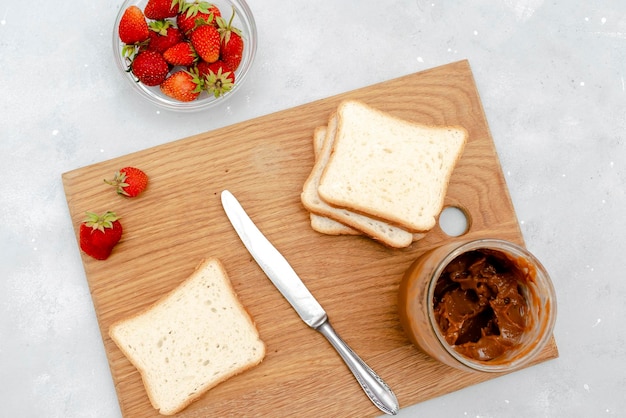 Sándwich de pan tostado con mantequilla de maní, fresas y nueces en una tabla de cortar de madera para niños, postre dulce para bebés, desayuno saludable, almuerzo, comida, arte sobre fondo gris, vista superior, plano