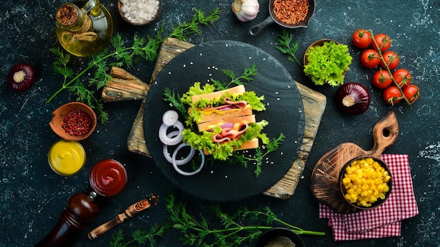 Sándwich de pan tostado con salchicha, cebolla, queso y lechuga sobre un fondo de piedra negra Comida callejera Espacio libre para copiar