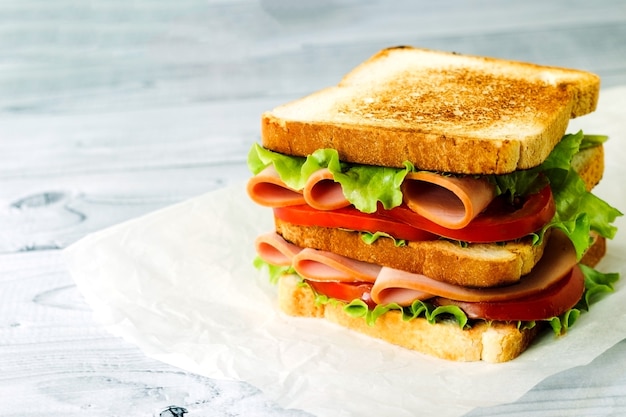 Sándwich de pavo de corte frío en trigo integral con tomate lechuga jamón sobre fondo de madera