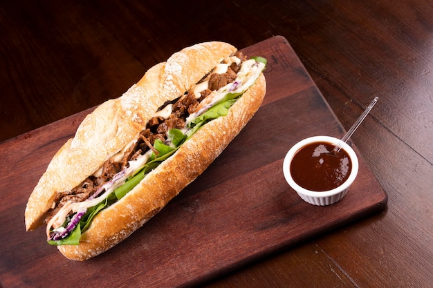 Foto sándwich de pechuga de res con rúcula y ensalada de col en pan baguette sobre tabla de madera con salsa de barbacoa en la vista superior de la esquina