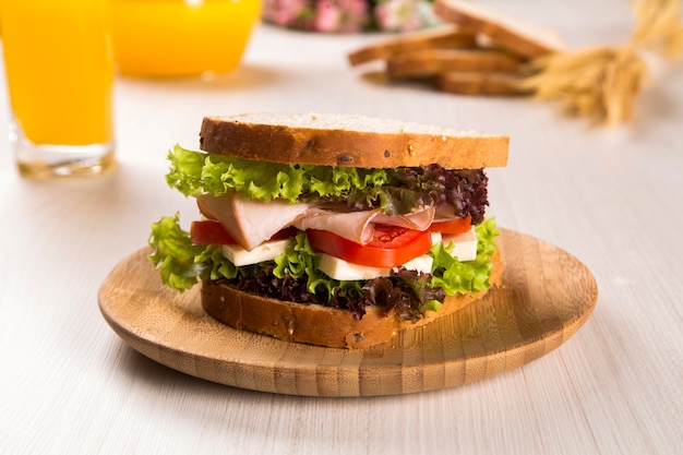 Sándwich en un plato blanco con pechuga de pavo, tomate, lechuga y queso sobre la mesa