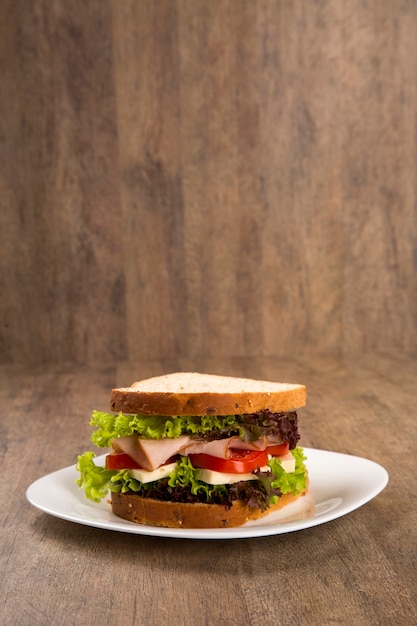 Sándwich en un plato blanco con pechuga de pavo, tomate, lechuga y queso sobre la mesa