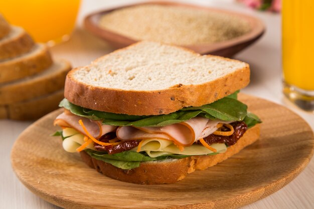 Sándwich en un plato blanco con pechuga de pavo, tomate, lechuga y queso sobre la mesa