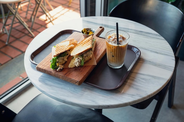 Sándwich de pollo con café helado en la mesa del café por la mañana