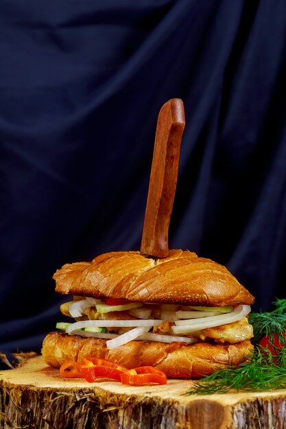 Sándwich de pollo con cebolla tomate pepino en un soporte de madera