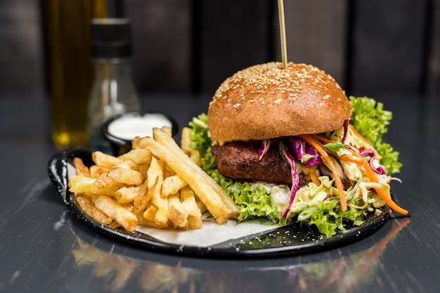 Sándwich de pollo frito con verduras y papas fritas en una mesa de madera