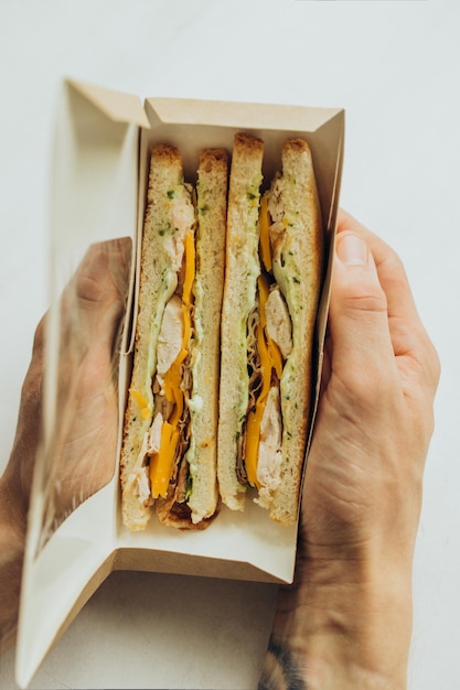 Sándwich con pollo y queso se sostiene en las manos en un paquete abierto