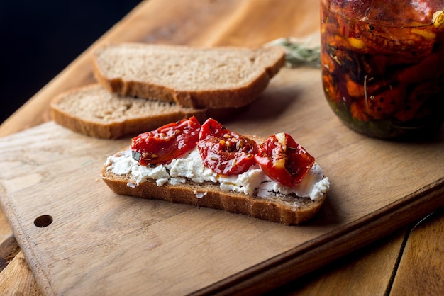 Sándwich con queso de cabra, tomates secos y tomillo servido en el tablero en una superficie de madera brillante