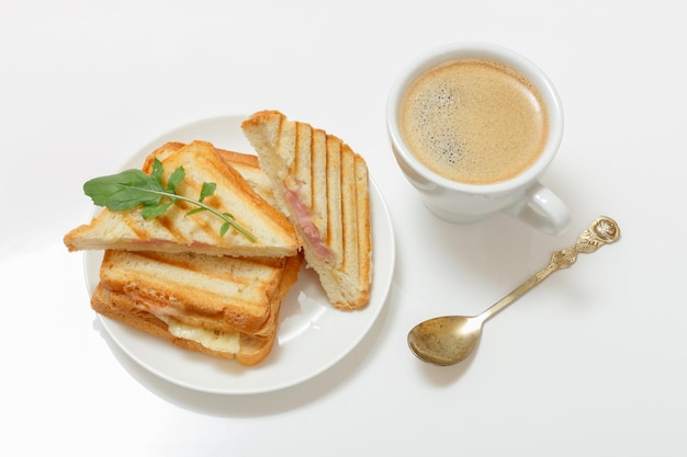 Sándwich de queso a la parrilla casero para el desayuno en un plato y una taza de café con una cuchara. Vista superior.