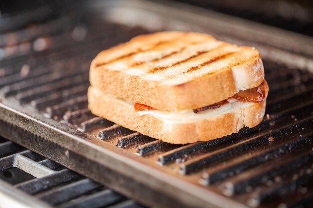 Sándwich de queso a la parrilla con tiras de tocino y tomate fresco en una parrilla de gas al aire libre.