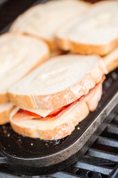 Sándwich de queso a la parrilla con tiras de tocino y tomate fresco en una parrilla de gas al aire libre.