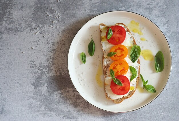 Sándwich de queso, tomate y albahaca en un plato de postre. La parte superior del sándwich se riega con mantequilla. Vista superior